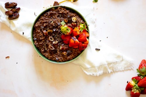A plate with the delicious chocolate oatmeal, dates and strawberries
