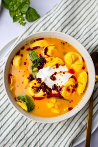 A bowl with the 4 ingredient tortellini soup. Garnished with cream cheese and siracha.