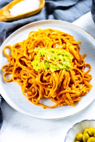 a plate with the most creamy vegan coconut pasta topped with a fresh chili avocado dip